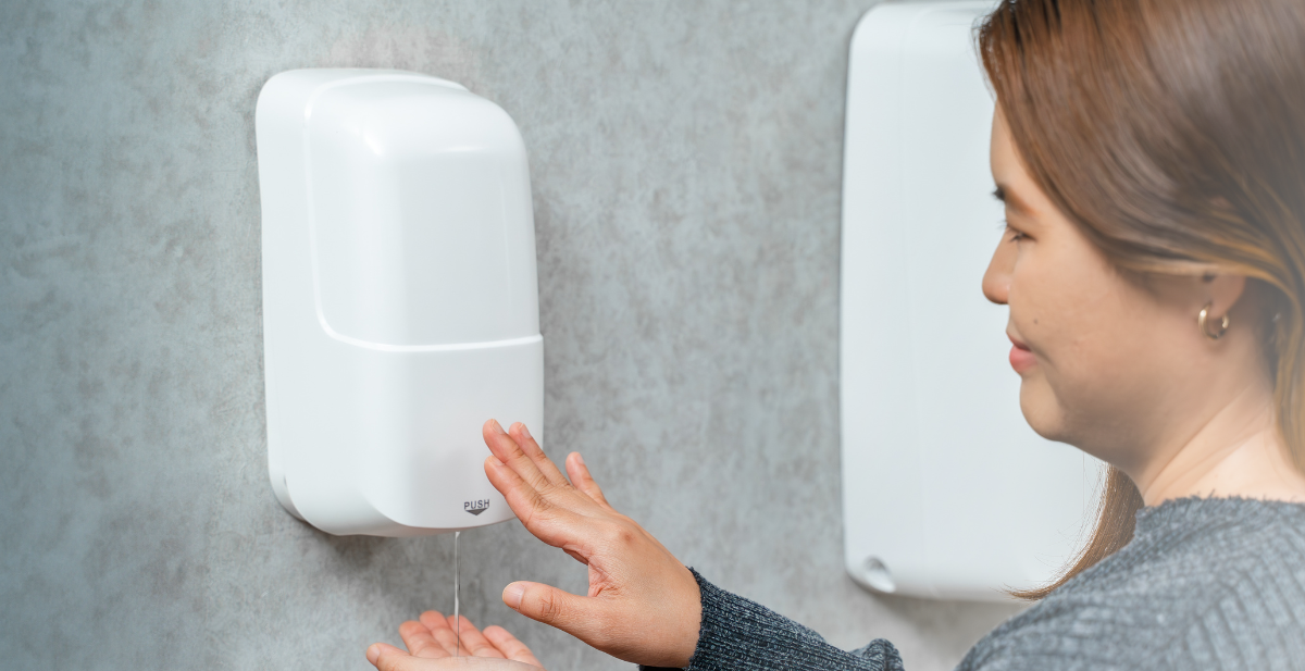 A person using an Initial Singapore hands-free sanitiser dispenser at an office entrance.