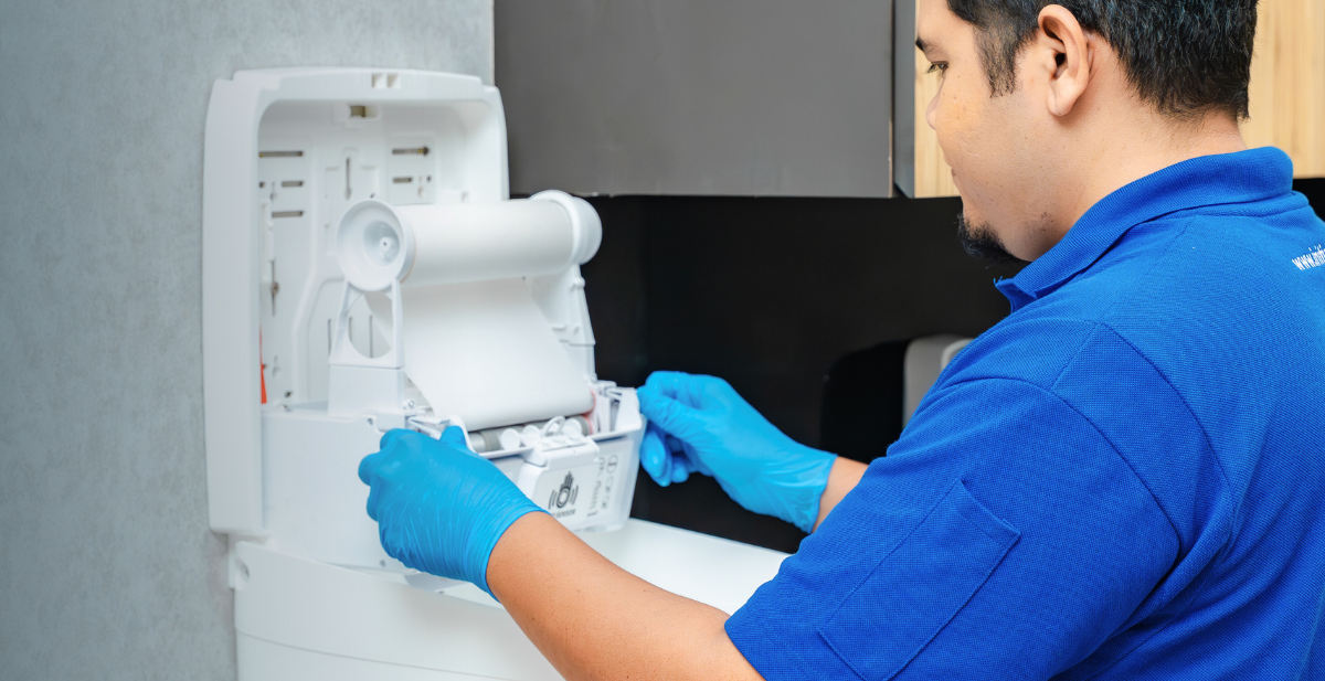 Technician installing sanitiser dispenser for workplace hygiene